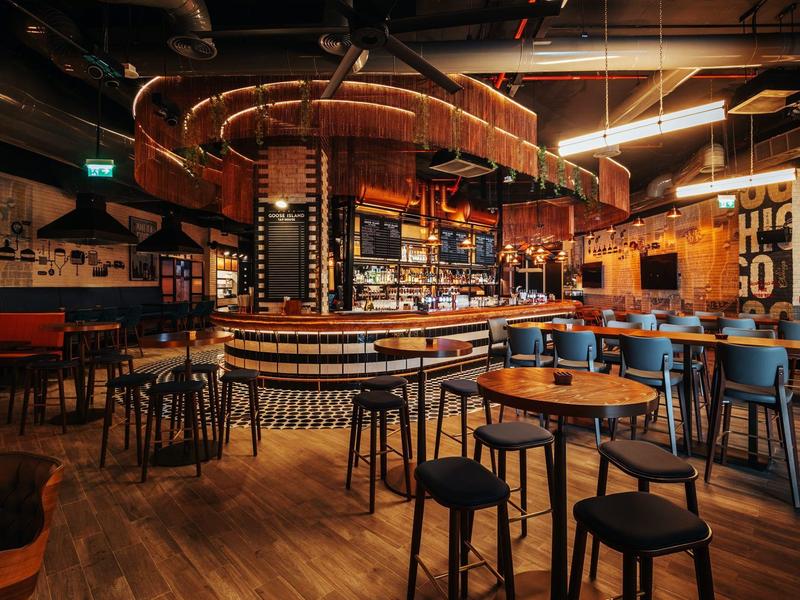 Gezellige hotelbar met ronde houten tafels, barkrukken en warm licht.