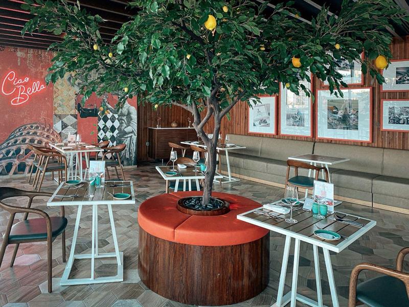 Gezellige binnenruimte met een boom in het midden omgeven door oranje banken en moderne tafels.