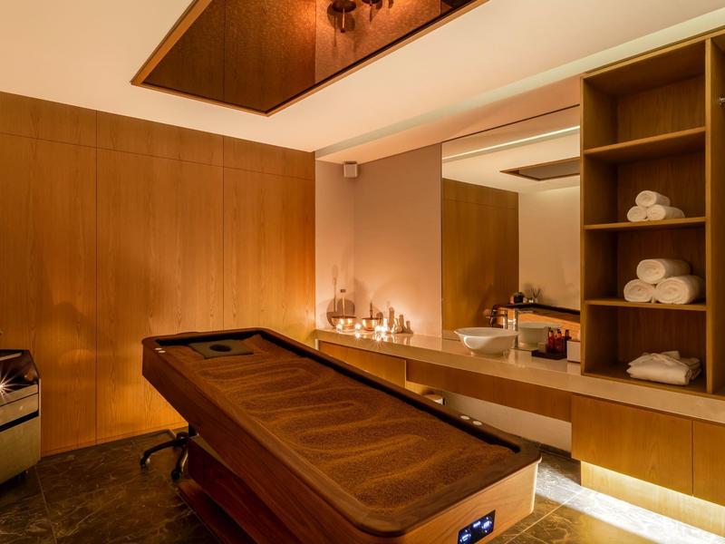 Gezellige wellnessruimte met massagetafel, warm licht en handdoeken op planken.