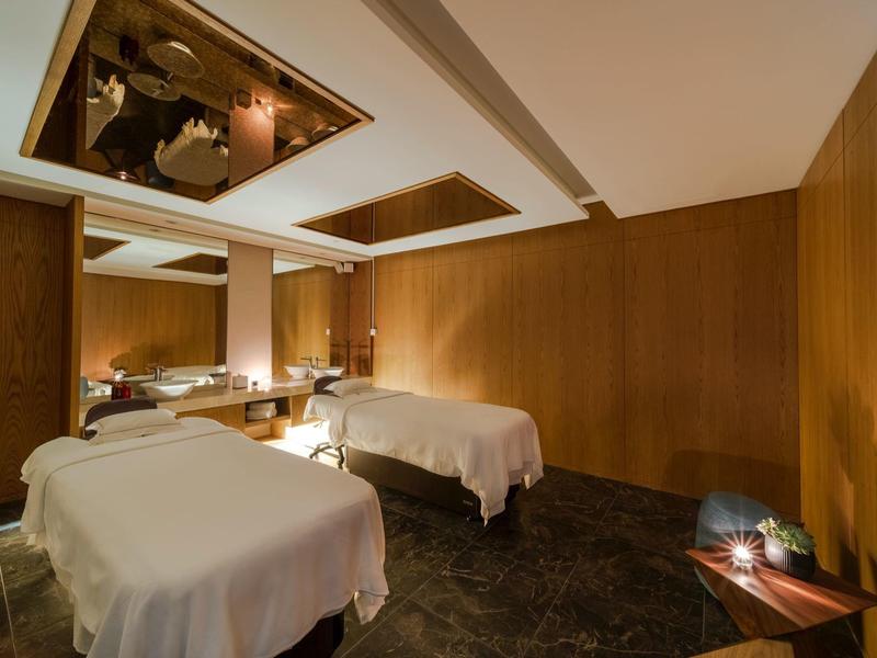 Een rustige massageruimte met twee witte bedden en warme houten inrichting.