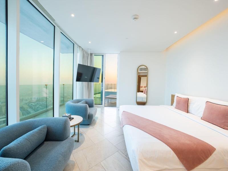 Licht hotelkamer met groot bed, zithoek en panoramische ramen met uitzicht.