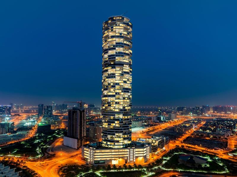 Een hoge, verlichte wolkenkrabber in een stad 's nachts met omringende straatverlichting.