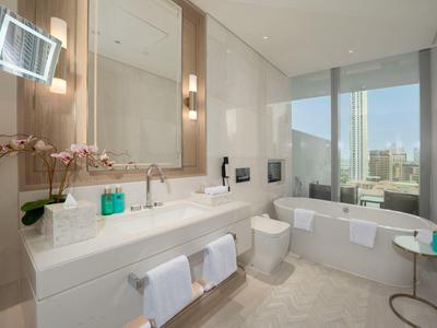 Modern hotel bathroom with large bathtub, double sink, and big window with city view.