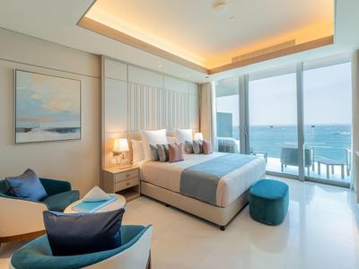 Bright bedroom with double bed, seating area, and balcony overlooking the sea.