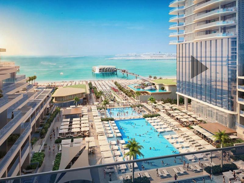 Modern hotel complex with outdoor pool and sea view under clear sky.