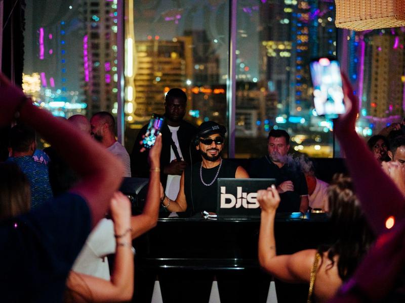 A DJ is playing at a late-night party in a high-rise club with city lights.