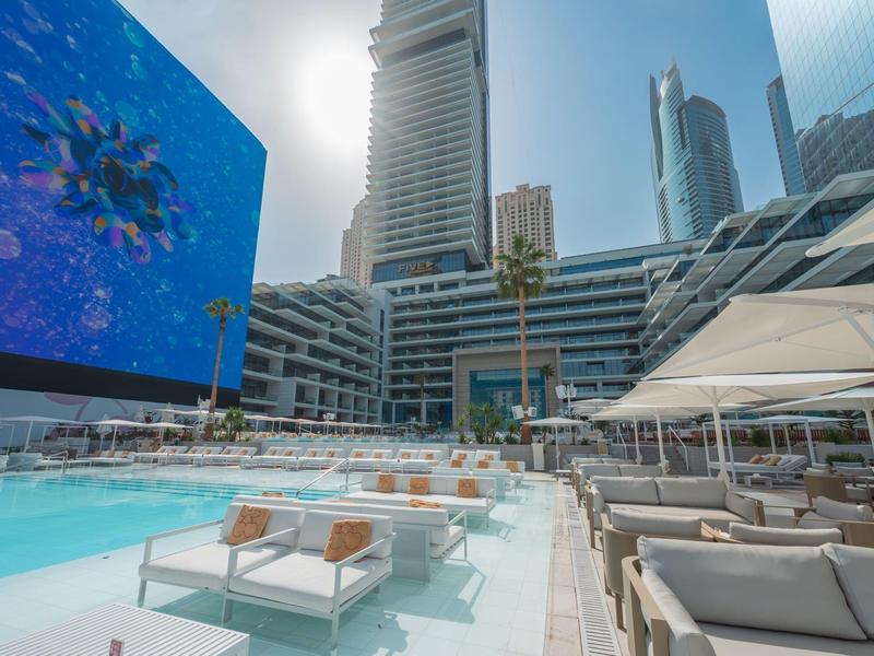 Modern outdoor pool area with loungers and skyscrapers in the background on a sunny day.