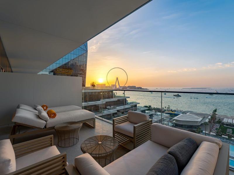 Balcony with modern lounge furniture overlooking the sea at sunset.