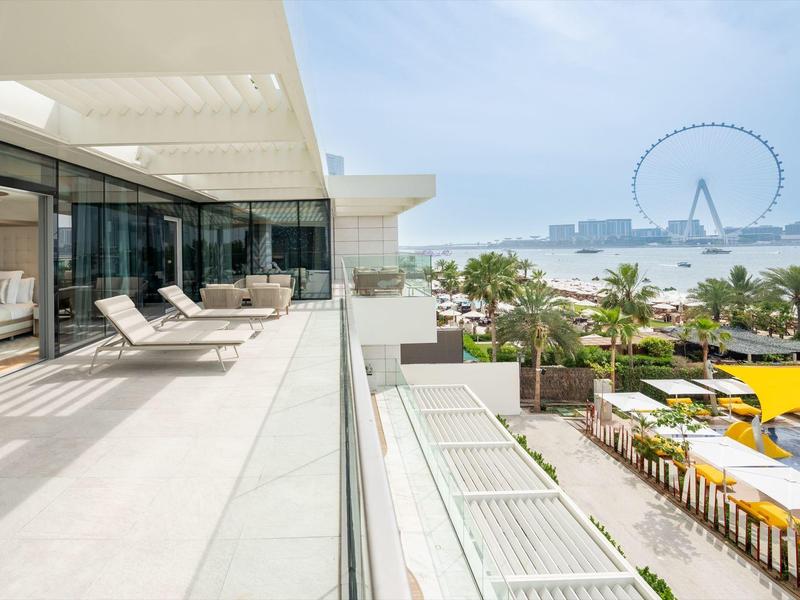 Modern terrace with lounge chairs overlooking city, water, and Ferris wheel on a sunny day.