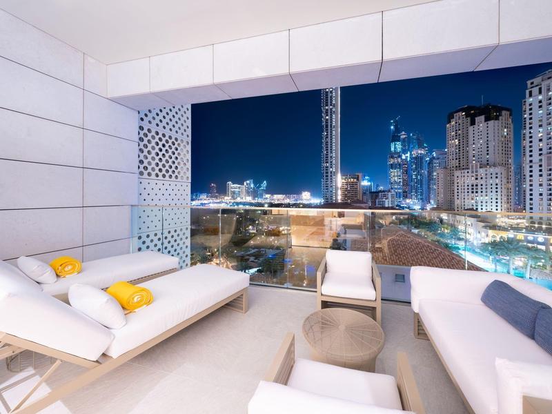 Modern balcony with comfortable white furniture and a view of the city at night.