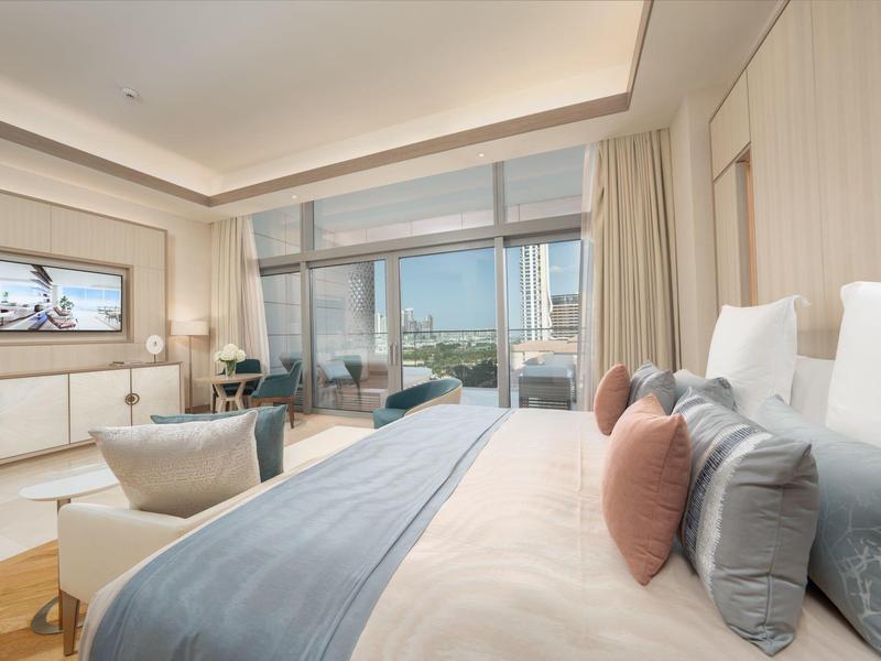 Bright hotel room with double bed, seating area, and large windows overlooking the city.