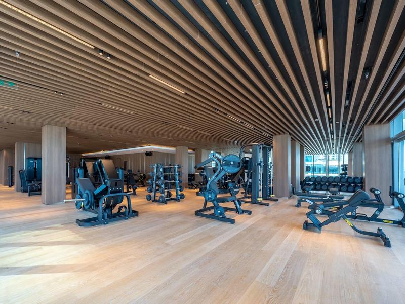 Large modern gym with wooden floor, black exercise machines, and big windows.