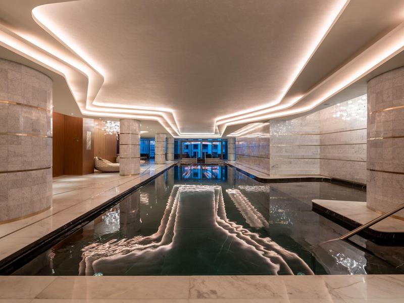 Modern indoor pool with white ceiling lights and marble floors in a hotel.