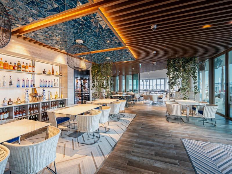 Modern hotel bar with stylish chairs, wooden ceiling, and large windows with a view.