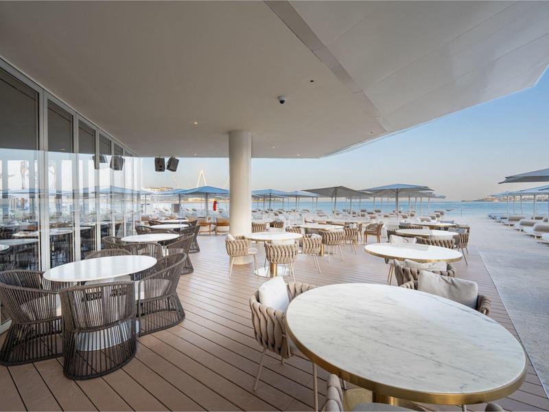 Open terrace with round tables and chairs overlooking the sea in bright daylight.