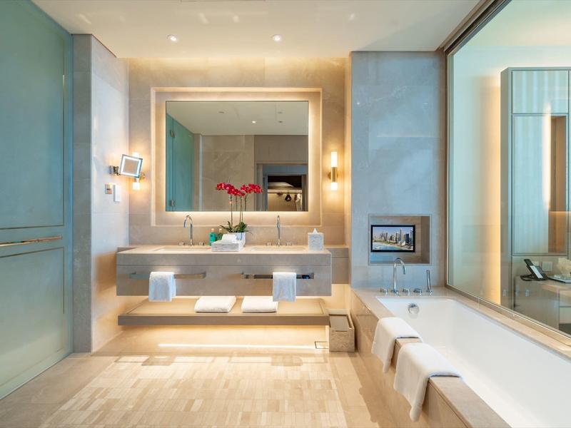Modern bathroom with large mirror, sink, and bathtub under warm lighting.