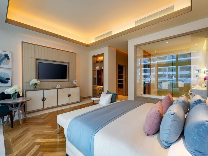 Modern hotel room with bed, TV, and large window.