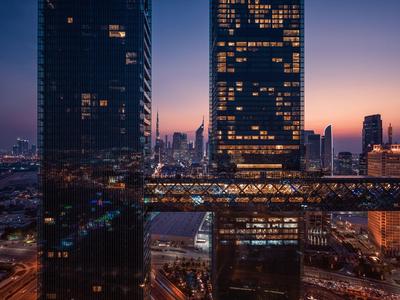 Dos rascacielos iluminados conectados por un puente peatonal al anochecer en la ciudad.