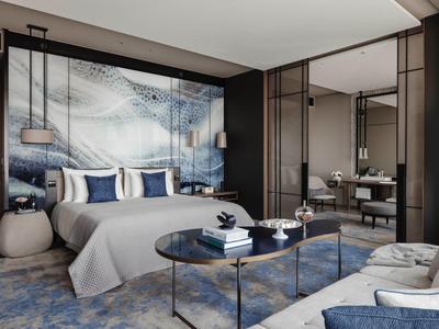 Modern hotel room with large bed, blue carpet, and stylish seating areas.
