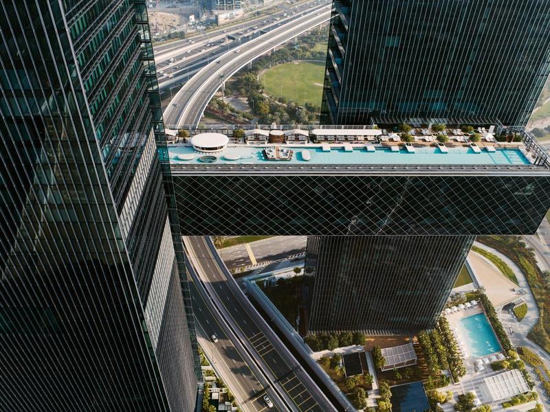 Infinity pool links two skyscrapers overlooking roads and city.