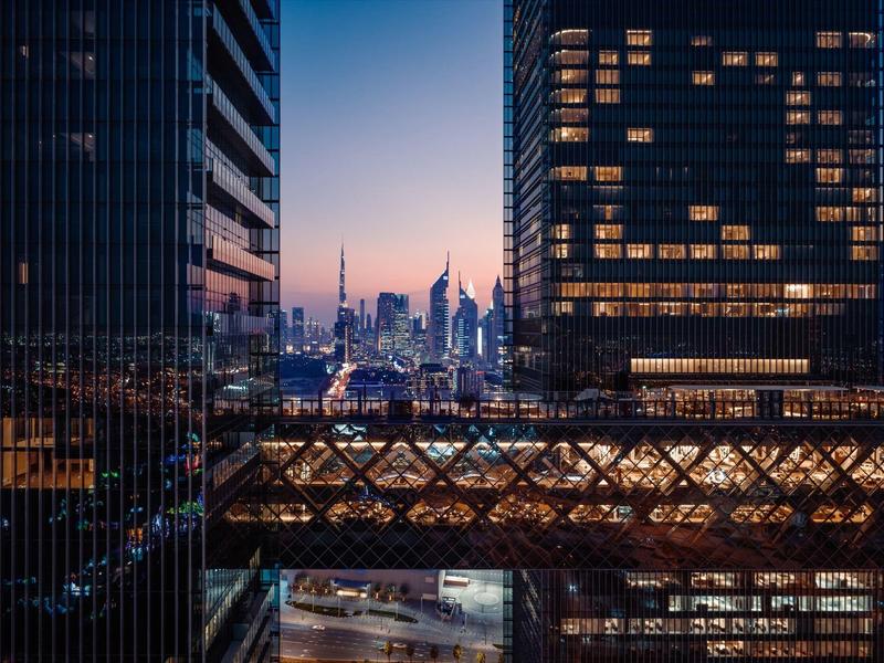 View between modern skyscrapers of a city at sunset with illuminated streets.