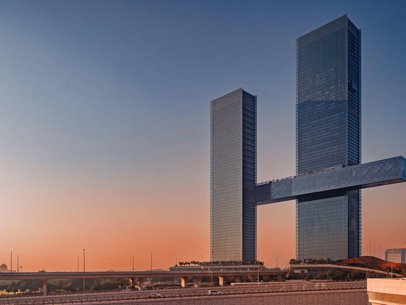 Modern skyscraper with two towers connected by a horizontal bridge at sunset.