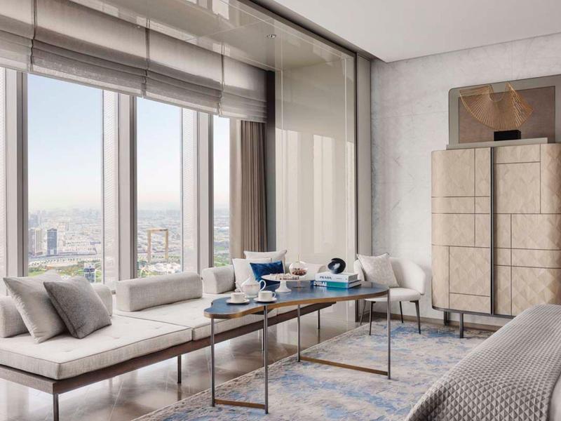 Bright hotel room with seating area, table, large window, and city view.