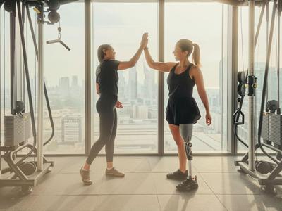Zwei Frauen geben sich im Fitnessstudio vor einem großen Fenster einen High-Five.