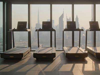 Vier Laufbänder in einem Fitnessraum mit Panoramablick auf die Stadt bei Sonnenaufgang.