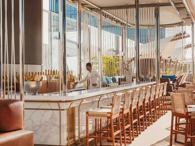 Moderner Barbereich mit Holzstühlen und hellem Marmortresen in einem sonnendurchfluteten Hotel.