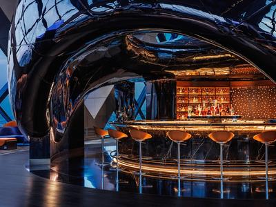 Moderní hotelový bar s zakřivenou černou stropní klenbou a stylovými barovými židlemi.