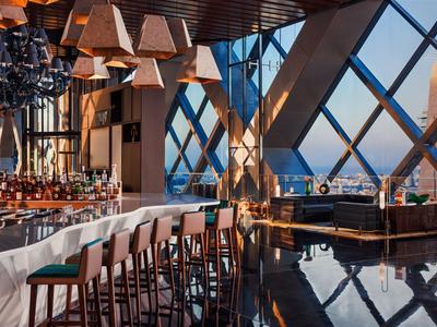 Moderní hotelový bar s vysokými stoličkami a velkými okny s výhledem na město