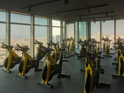 Innenraum eines Fitnessraums mit vielen gelben Spinning-Fahrrädern und Panoramafenstern mit Stadtblick