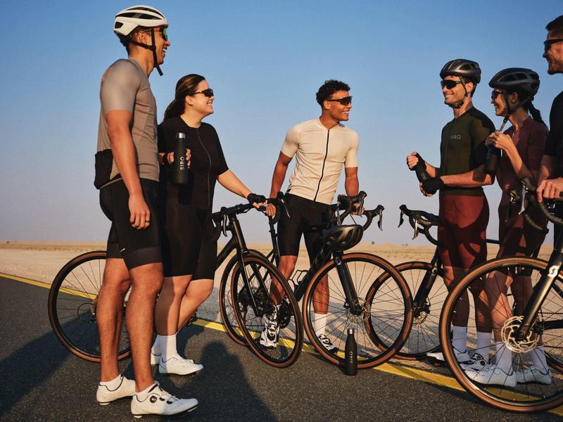Group of cyclists standing with their bikes on a road, chatting in sunny weather.