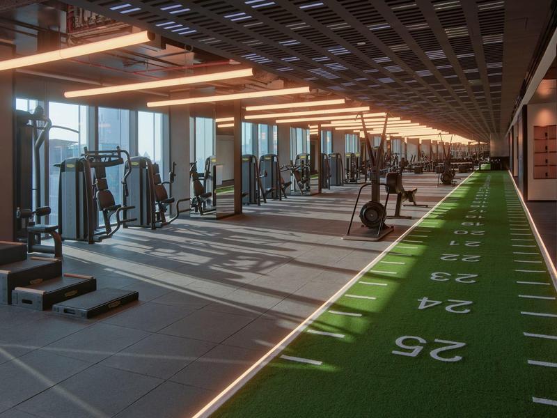 Long modern gym with strength equipment and a green training field with markings.