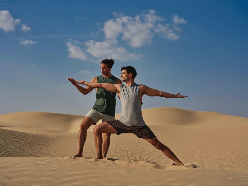 Two men practicing yoga in the desert under a clear sky.