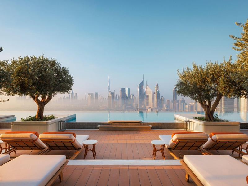 Pool area with lounge chairs and trees overlooking a skyline under a clear sky