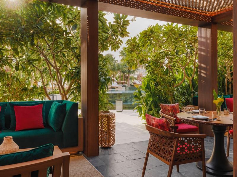 Covered terrace with seating area, greenery, and water view in a hotel setting.