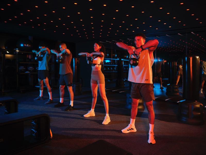Four people doing fitness exercises in a dimly lit gym.