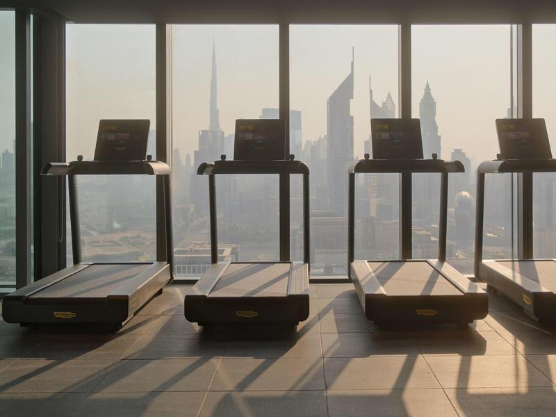 Four treadmills stand before large windows overlooking a city with tall skyscrapers.