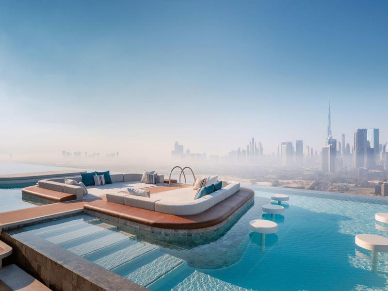 Modern infinity pool with sun loungers and skyline view under clear sky.