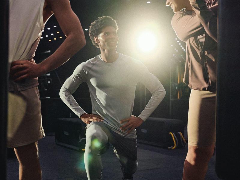 Coach motivates young basketball players in a gym with ceiling lights.