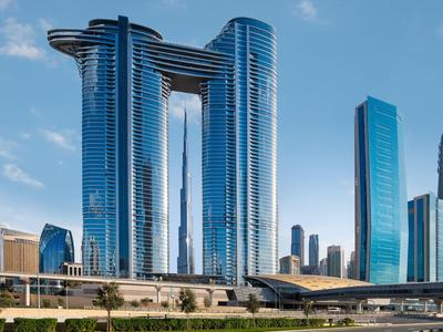 Moderne gläserne Wolkenkratzer vor blauem Himmel mit breiter Straße und Grünflächen im Vordergrund.