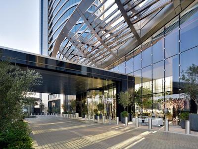 Entrée d'hôtel moderne avec façade en verre, auvent et plantes à l'entrée.