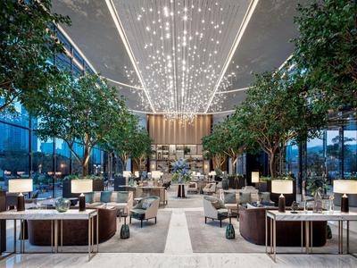 Espace lounge d'hôtel luxueux avec des arbres et un éclairage moderne dans un bâtiment en verre.
