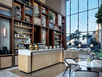 Modernes Café mit hoher Glasfassade, hellen Holzmöbeln und gemütlichen Sitzbereichen.