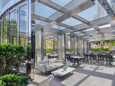 Moderner Wintergarten mit Glasdach, Metallrahmen und bequemen Sitzmöbeln im Außenbereich.