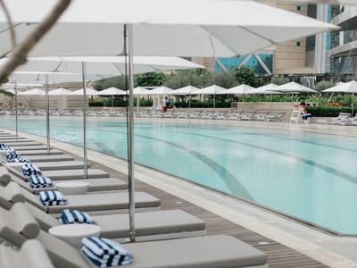 Longue piscine extérieure avec transats et parasols blancs dans un espace hôtelier.