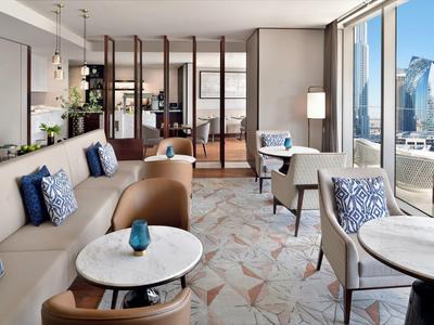 Moderner Wohnraum mit beigen Sofas, blauen Kissen, runden Tischen und großen Fenstern zur Stadtseite.