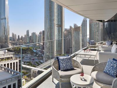 Großer Balkon mit modernen Sitzmöbeln, Glasgeländer und Blick auf Wolkenkratzer bei klarem Himmel.